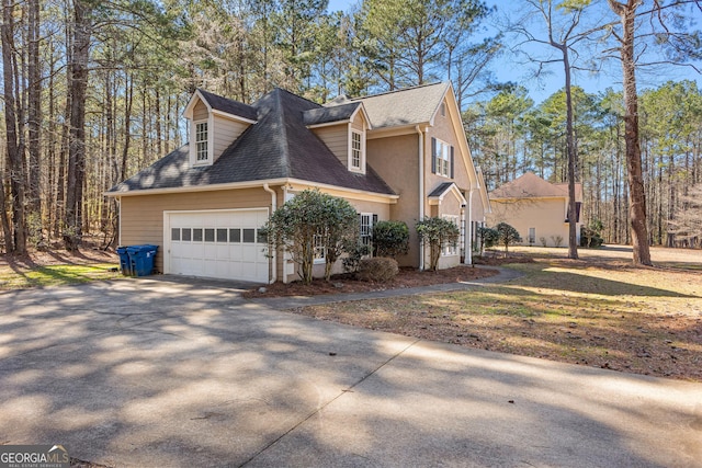 view of side of property featuring a shingled roof, driveway, an attached garage, and stucco siding