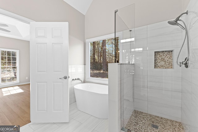 full bathroom featuring vaulted ceiling, a stall shower, a soaking tub, and tile walls