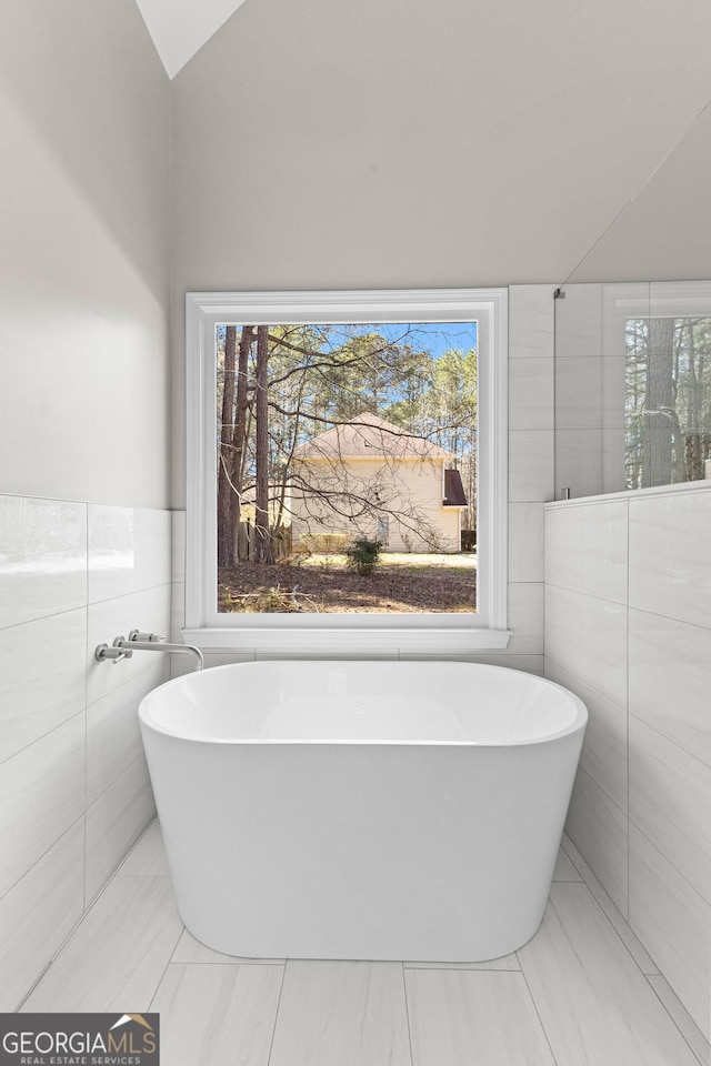 full bathroom featuring a freestanding tub, vaulted ceiling, and tile walls