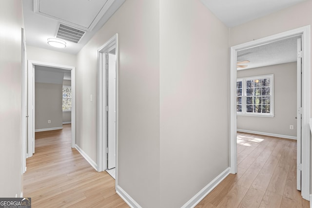 hallway with light wood finished floors, visible vents, and baseboards