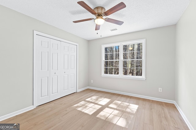 unfurnished bedroom with light wood-style flooring, a textured ceiling, baseboards, and a closet