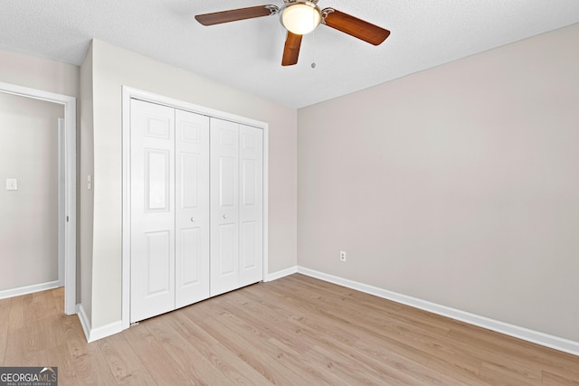 unfurnished bedroom featuring ceiling fan, a textured ceiling, baseboards, light wood-style floors, and a closet