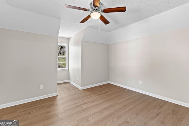 empty room featuring baseboards, ceiling fan, vaulted ceiling, a textured ceiling, and light wood-style floors