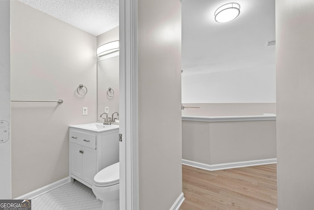 bathroom with a textured ceiling, toilet, wood finished floors, vanity, and baseboards