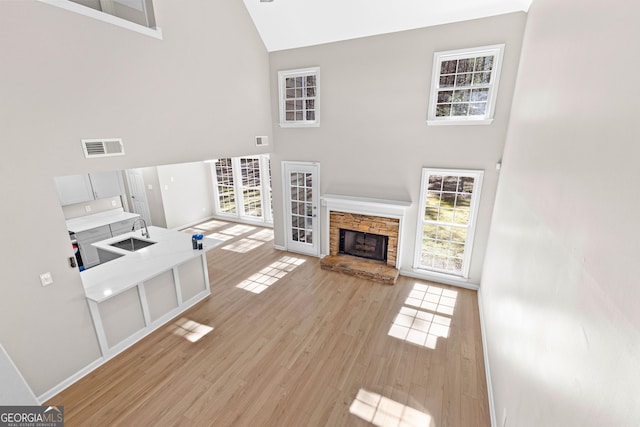 unfurnished living room with light wood-type flooring, visible vents, high vaulted ceiling, and a stone fireplace