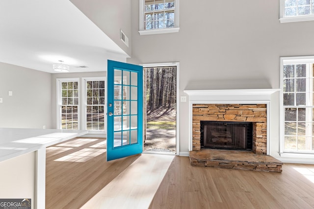 unfurnished living room featuring a high ceiling, visible vents, wood finished floors, and a stone fireplace