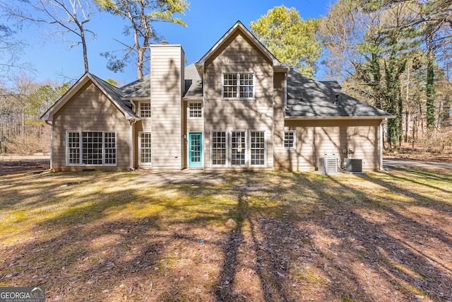 back of house featuring roof with shingles, a chimney, central AC, and a yard