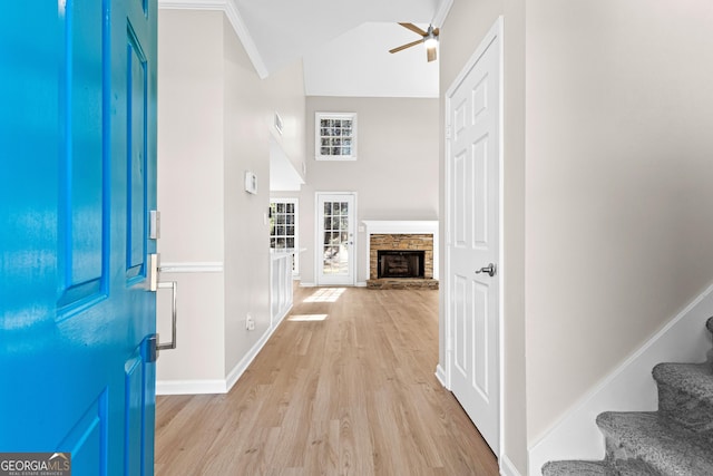 foyer entrance with baseboards, stairs, light wood-type flooring, a fireplace, and high vaulted ceiling