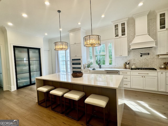 kitchen featuring gas stovetop, white cabinetry, premium range hood, and ornamental molding