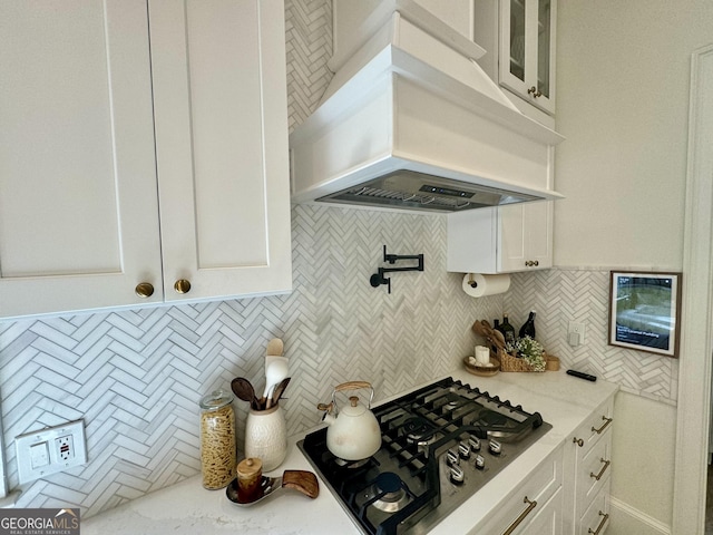 kitchen featuring white cabinets, glass insert cabinets, light stone countertops, custom exhaust hood, and stainless steel gas cooktop