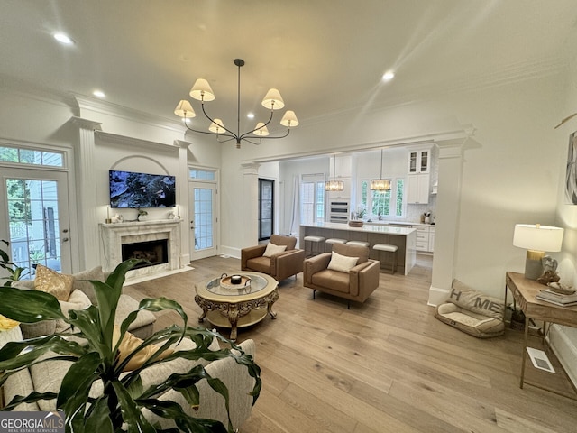 living area with light wood-style floors, a chandelier, a fireplace, and crown molding