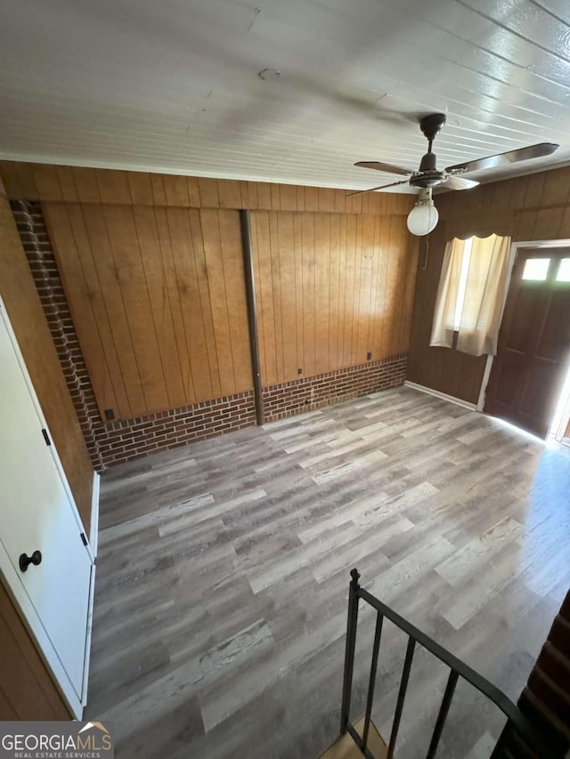 spare room with a ceiling fan, light wood-style flooring, and wooden walls