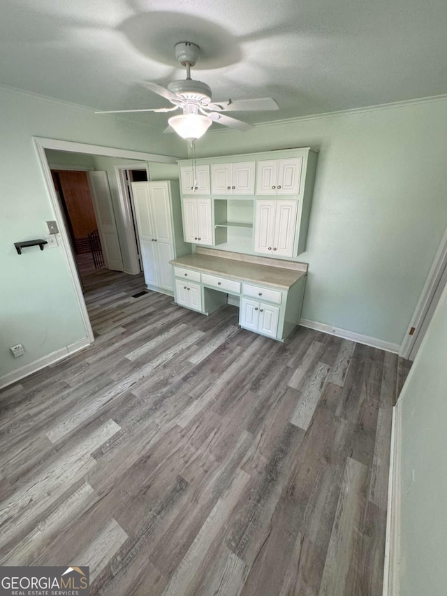 interior space featuring baseboards, built in study area, ceiling fan, ornamental molding, and wood finished floors