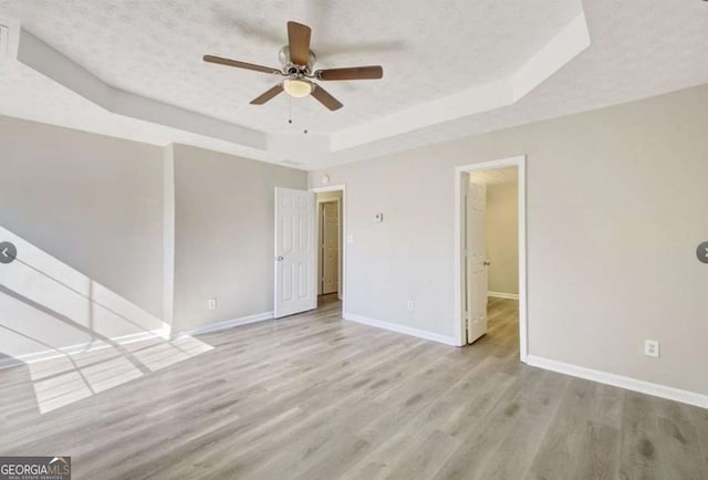 unfurnished room featuring a raised ceiling, wood finished floors, baseboards, and a textured ceiling