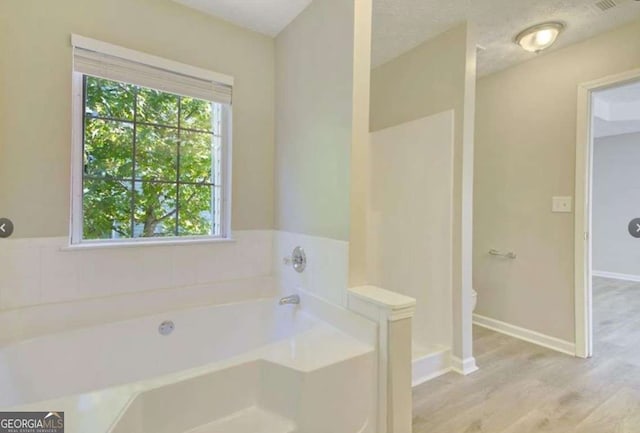 bathroom with baseboards, toilet, wood finished floors, a bath, and a textured ceiling