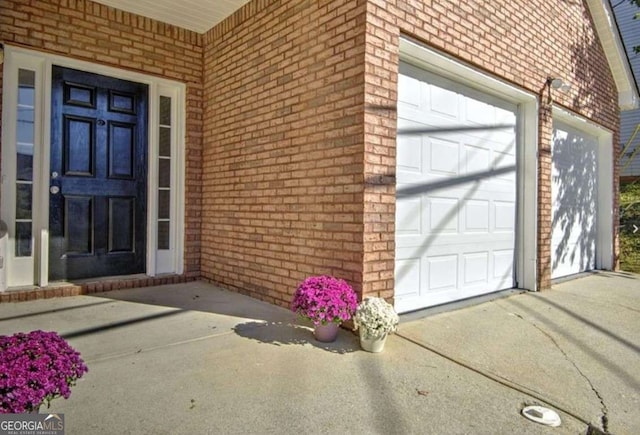 doorway to property featuring an attached garage and brick siding