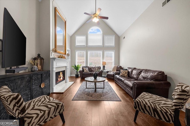 living area with ceiling fan, high vaulted ceiling, visible vents, a lit fireplace, and dark wood finished floors