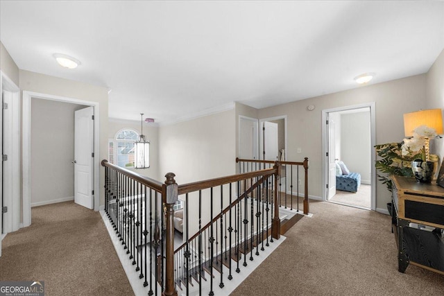 hall with carpet floors, baseboards, and an upstairs landing