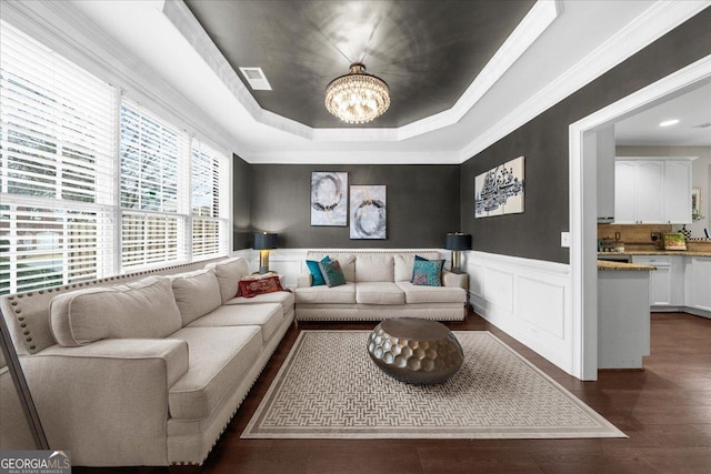 living area with dark wood-style flooring, a wainscoted wall, a raised ceiling, visible vents, and an inviting chandelier