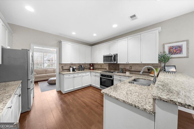 kitchen with stainless steel appliances, backsplash, a sink, light stone countertops, and a peninsula