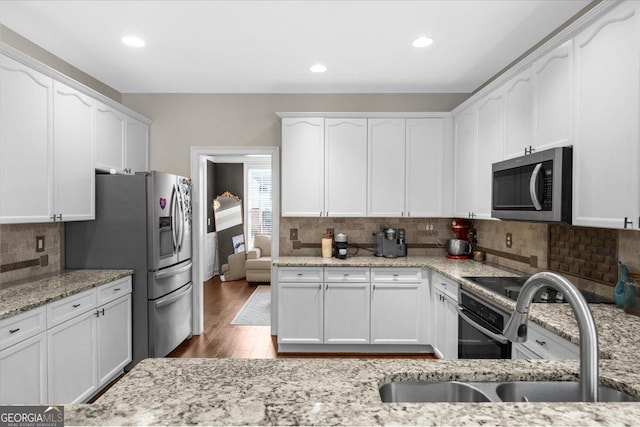 kitchen with stainless steel appliances, wood finished floors, a sink, and white cabinetry