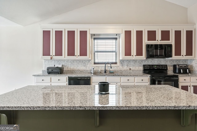 kitchen with black appliances, a sink, light stone counters, decorative backsplash, and vaulted ceiling