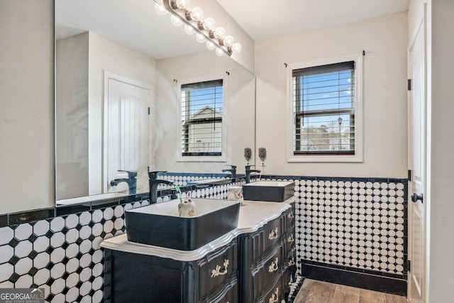 bathroom with wainscoting, wood finished floors, tile walls, and a sink