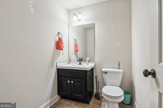 half bathroom featuring toilet, vanity, baseboards, and wood finished floors