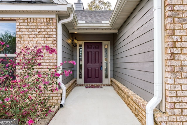 doorway to property with brick siding, a chimney, and roof with shingles