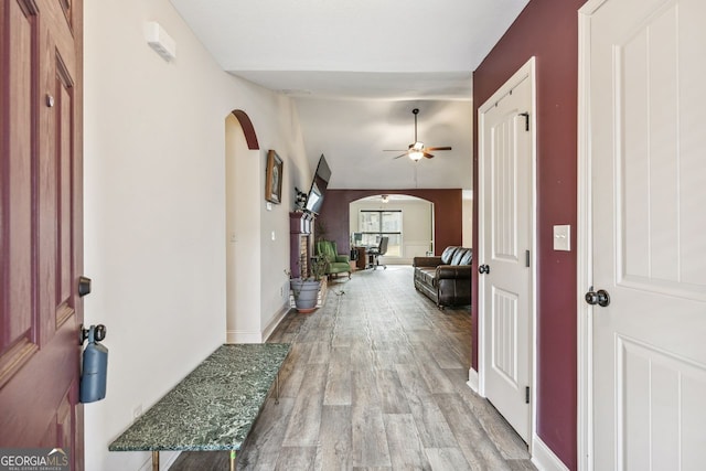 corridor with light wood-type flooring, arched walkways, baseboards, and vaulted ceiling