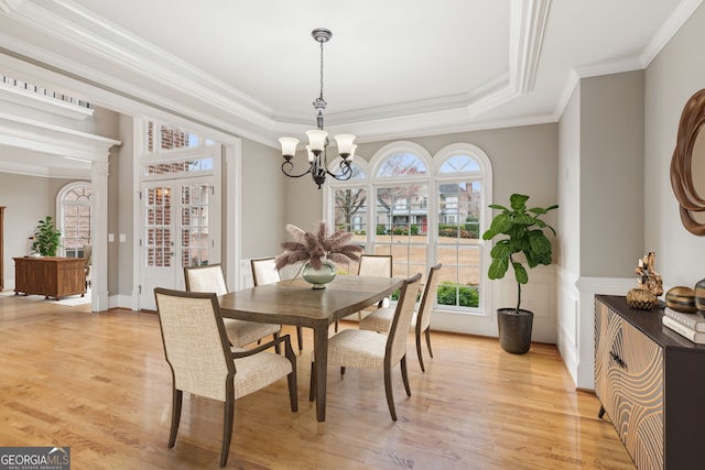 dining space featuring a notable chandelier, light wood-type flooring, and a raised ceiling