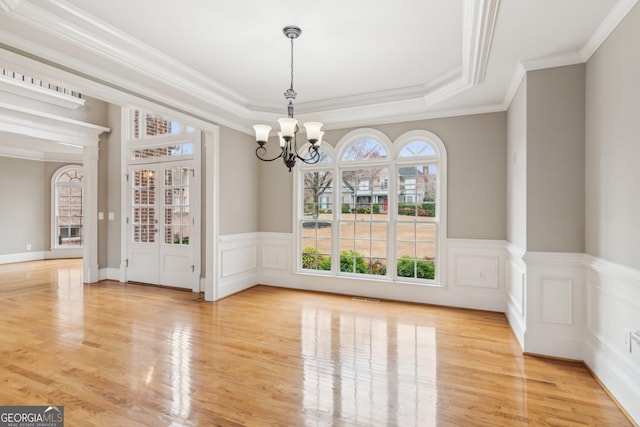 unfurnished dining area featuring light wood-type flooring, a tray ceiling, visible vents, and a chandelier