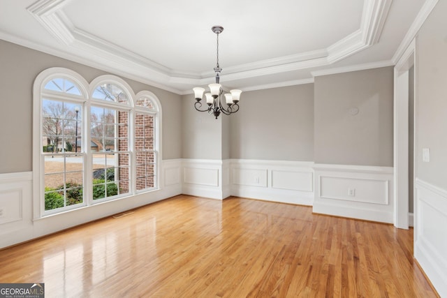 spare room with visible vents, a notable chandelier, light wood-style flooring, wainscoting, and a raised ceiling