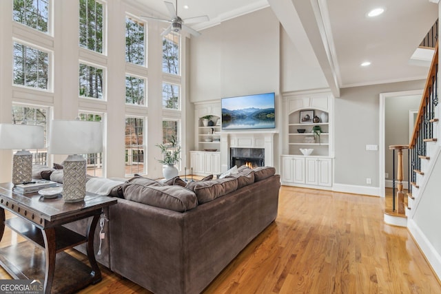 living room with stairway, light wood-style floors, ornamental molding, and a high end fireplace