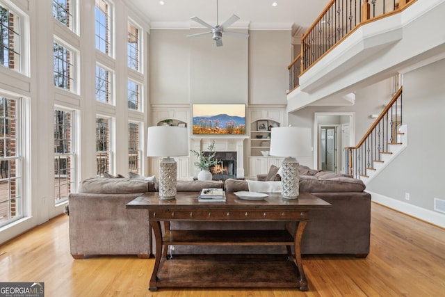 living area featuring light wood finished floors, baseboards, ceiling fan, ornamental molding, and a fireplace