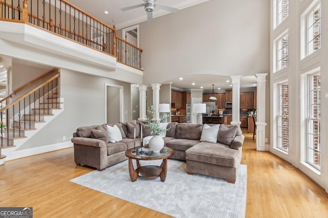 living room featuring light wood finished floors, stairway, baseboards, and decorative columns