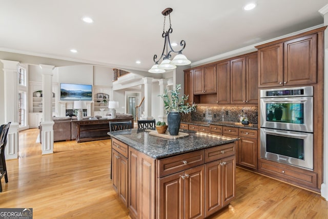 kitchen featuring double oven, ornamental molding, light wood-style flooring, a fireplace, and ornate columns