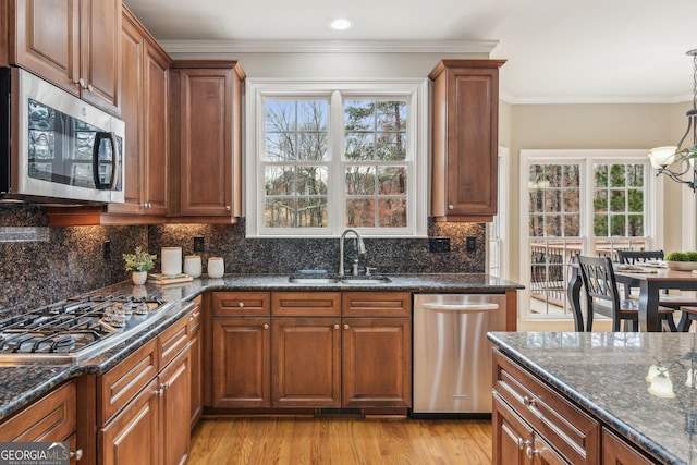 kitchen featuring light wood-style flooring, a sink, appliances with stainless steel finishes, crown molding, and decorative backsplash