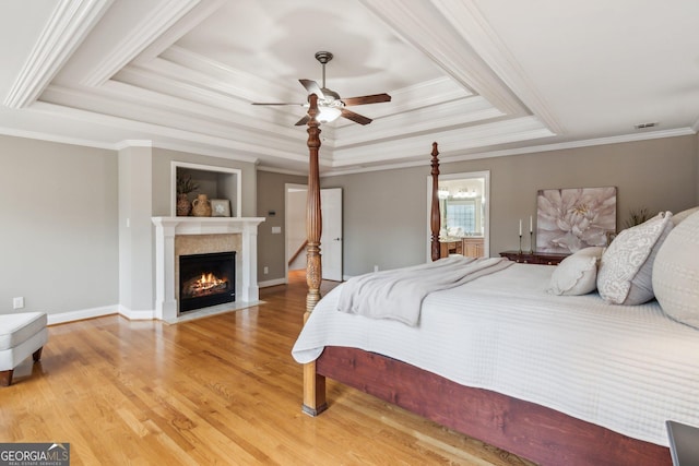 bedroom with a raised ceiling, wood finished floors, baseboards, and a warm lit fireplace