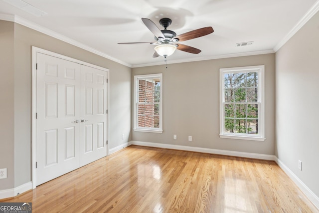 unfurnished bedroom with baseboards, visible vents, ornamental molding, light wood-style floors, and a closet