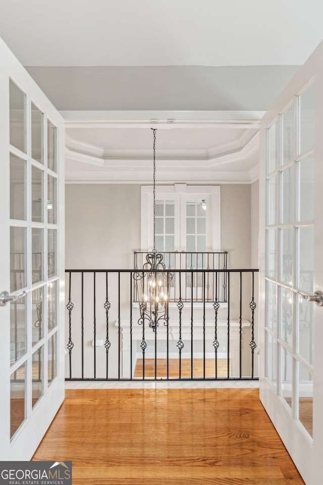 corridor with crown molding, a raised ceiling, an inviting chandelier, and wood finished floors