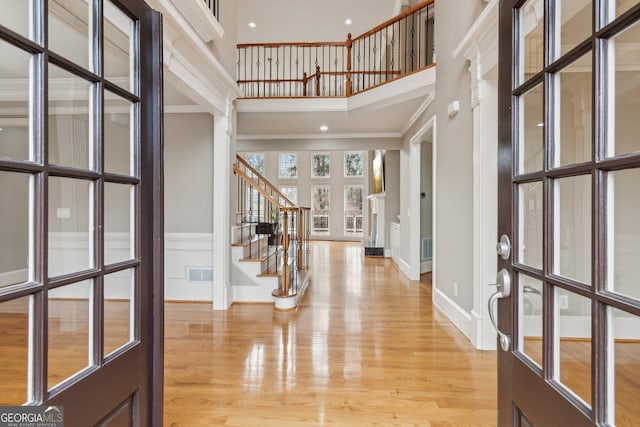 entrance foyer with visible vents, baseboards, stairs, a high ceiling, and light wood-style floors