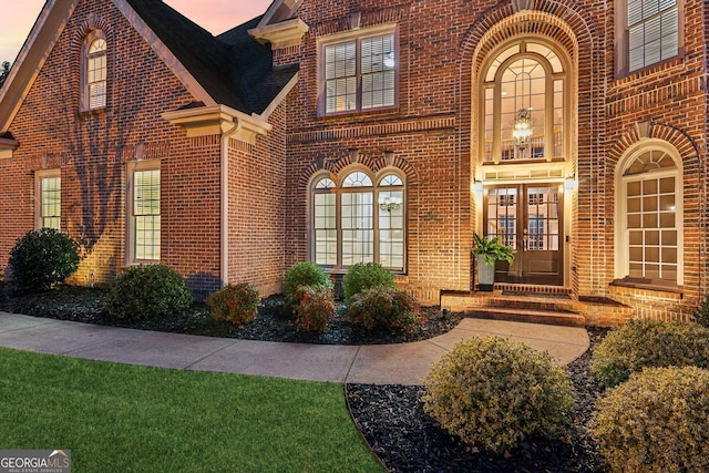 exterior entry at dusk featuring brick siding and french doors