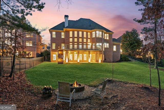 back of house at dusk featuring a fenced backyard, a fire pit, a lawn, and a deck