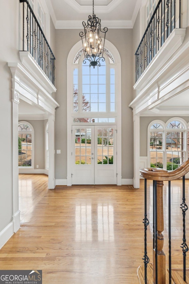 foyer entrance with crown molding, wood finished floors, french doors, a towering ceiling, and an inviting chandelier