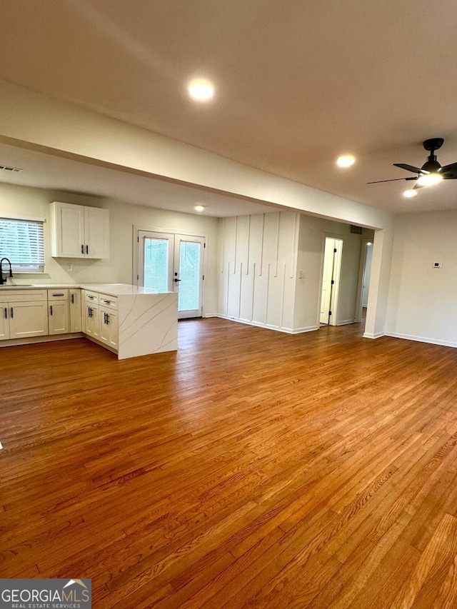 unfurnished living room with ceiling fan, a sink, wood finished floors, and plenty of natural light