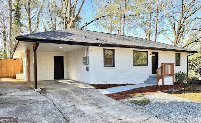 single story home with fence, roof with shingles, concrete driveway, an attached carport, and brick siding