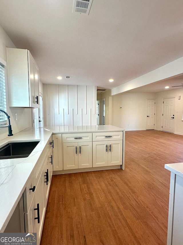 kitchen with visible vents, light wood-style flooring, open floor plan, white cabinetry, and a sink