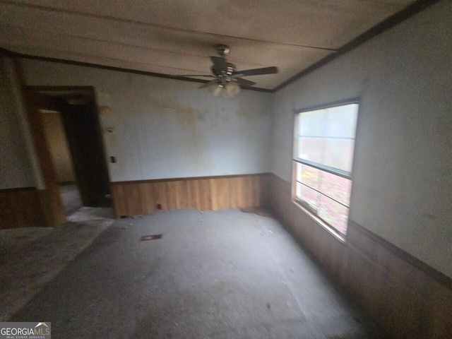 unfurnished room with wainscoting, wood walls, and ceiling fan