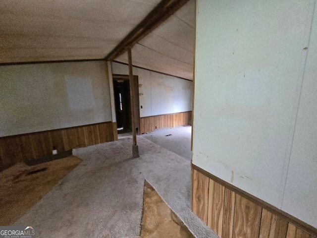 carpeted spare room with lofted ceiling with beams, wood walls, and wainscoting